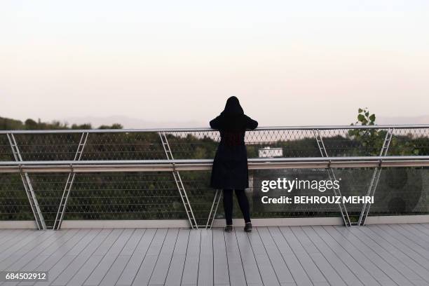 Picture taken on May 18, 2017 shows a woman looking at the skyline of northern Tehran from the "Nature" bridge in the capital Tehran on the eve of...
