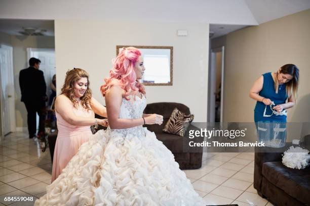 mother and friend helping young woman get dressed in gown for quinceanera - quinceañera fotografías e imágenes de stock
