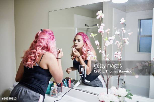 young woman putting on makeup in bathroom mirror while preparing for quinceanera - dyed hair - fotografias e filmes do acervo