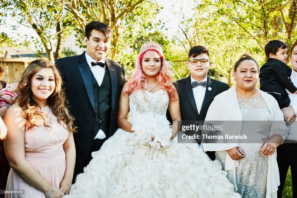 Young woman dressed in quinceanera gown standing in backyard surrounded by family