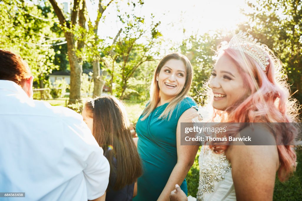 Laughing mother standing with family and daughter in backyard before quinceanera