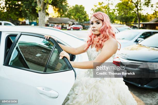 Young woman in gown standing by car before quinceanera