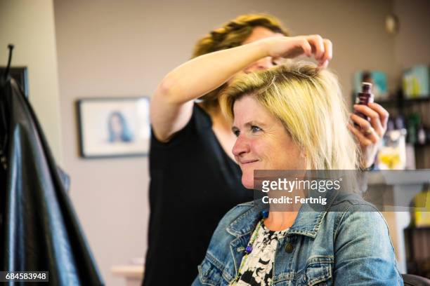 mature, middle-aged woman in a hair salon with a slightly pleased expression. - older woman colored hair stock pictures, royalty-free photos & images