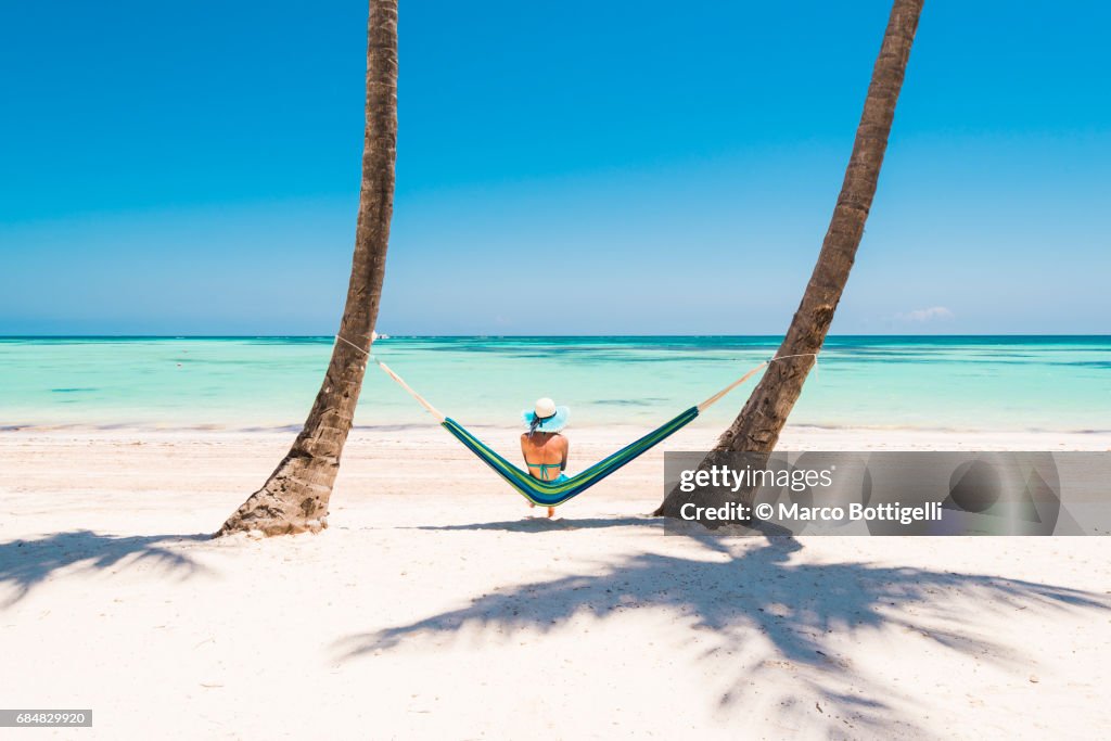Caucasian woman lying on hammock on a tropical beach.