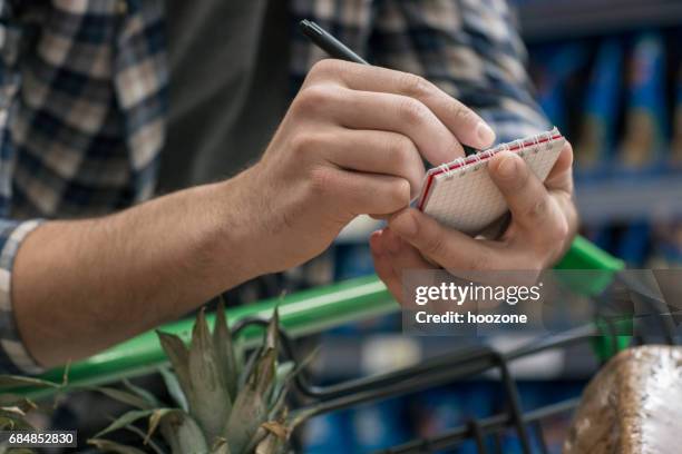 man hand holding shopping list in a supermarket - shopping list stock pictures, royalty-free photos & images