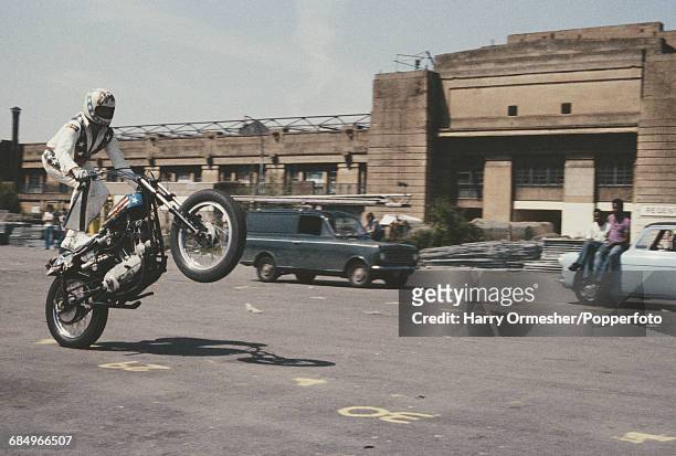 American stunt motorcyclist and entertainer Evel Knievel pictured performing a wheelie whilst riding on the back of his motorcycle in front of the...