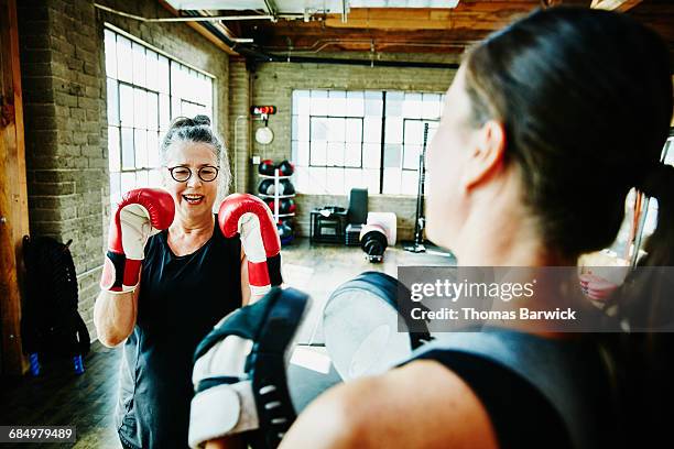 laughing mature woman boxing with coach in gym - boxeo deporte fotografías e imágenes de stock