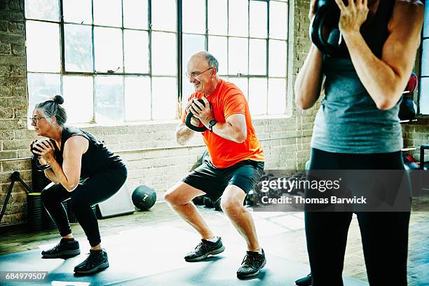 senior athletes doing kettlebell squats - 3 gym stock pictures, royalty-free photos & images