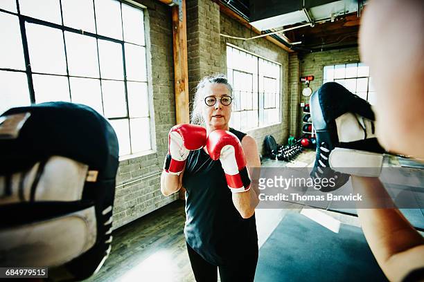 mature woman boxing with coach in gym - boxing training stock-fotos und bilder