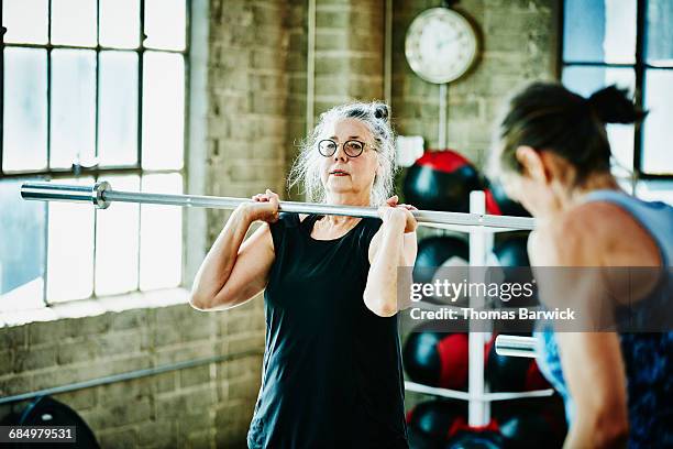 senior woman doing barbell lifts during workout - 50 60 jahre brille stock-fotos und bilder