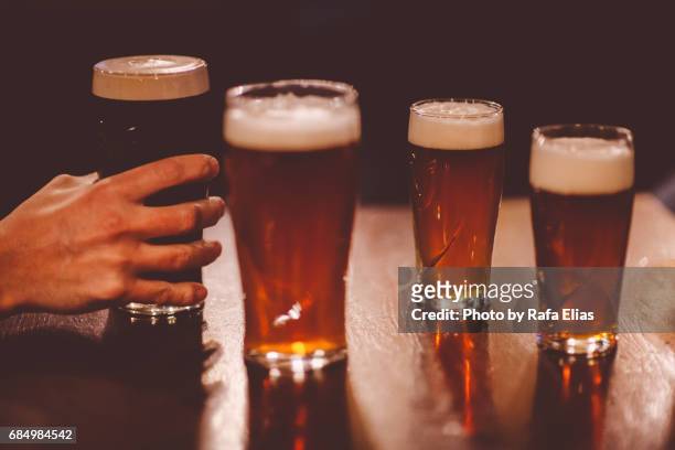 human hand grabbing pint of stout between some others pints of beer - beer stout stock-fotos und bilder