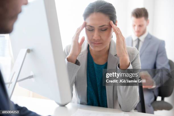 businesswoman with headache rubbing temples in office - verdruss stock-fotos und bilder