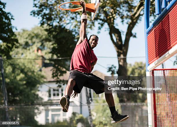 portrait of young male basketball player hanging from basketball hoop - man hanging stock pictures, royalty-free photos & images