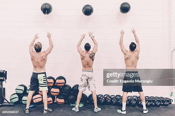 rear view of three male cross trainers throwing exercise balls in gym - cross trainer stock-fotos und bilder