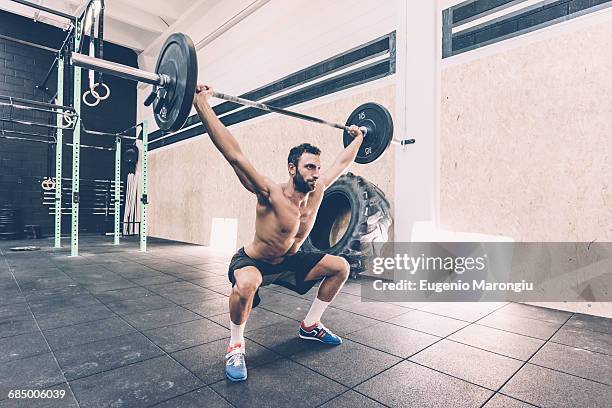 young man weightlifting barbell in cross training gym - snatch stockfoto's en -beelden