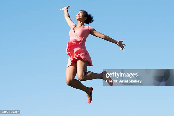mixed race woman jumping for joy in blue sky - euphoric female stock-fotos und bilder