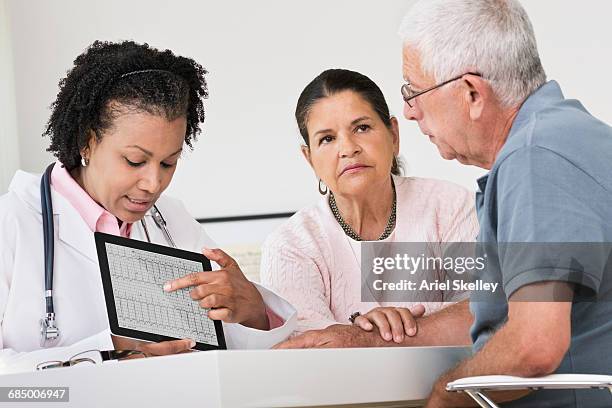 doctor showing pulse trace on digital tablet to patients - doctoring stock pictures, royalty-free photos & images