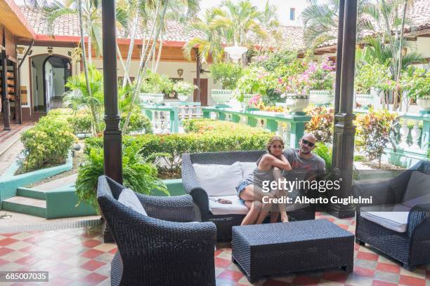 smiling caucasian couple on sofa in hotel courtyard - alberto guglielmi imagens e fotografias de stock