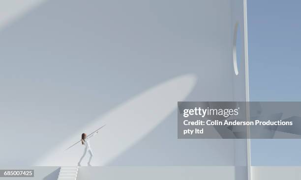 pacific islander woman aiming javelin at hole high on wall - aiming concept stock pictures, royalty-free photos & images