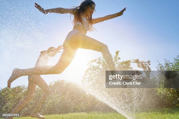 caucasian girls running and jumping through backyard sprinkler - atmosphere filter stock pictures, royalty-free photos & images