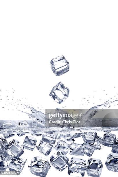 falling ice cubes splashing into water and floating - cubetto di ghiaccio foto e immagini stock