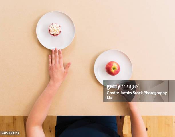 caucasian woman choosing apple instead of cupcake at table - mittlerer teil stock-fotos und bilder