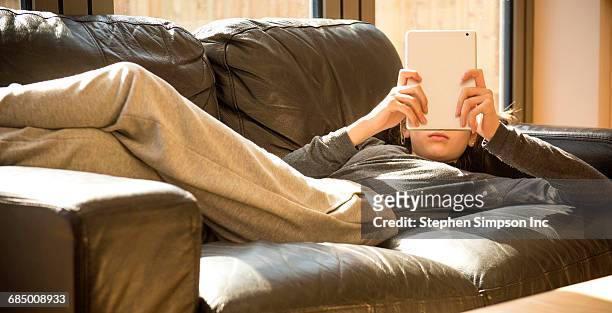 girl laying on sofa reading digital tablet - viso nascosto foto e immagini stock