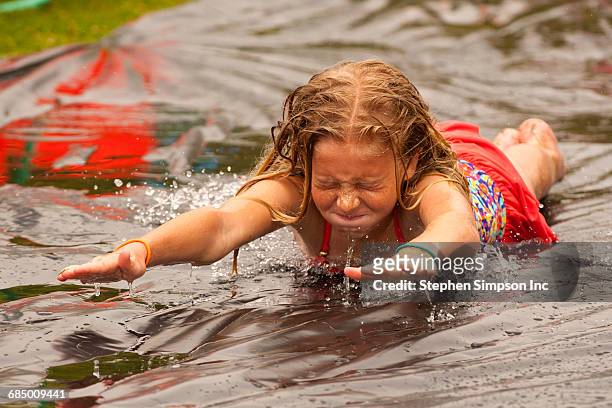 caucasian girl sliding in water on outdoor plastic tarp - plane stock-fotos und bilder
