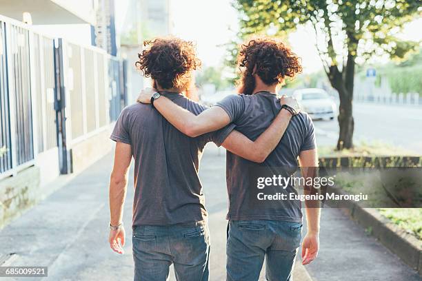 rear view of identical male adult twins strolling on sidewalk - zwilling stock-fotos und bilder