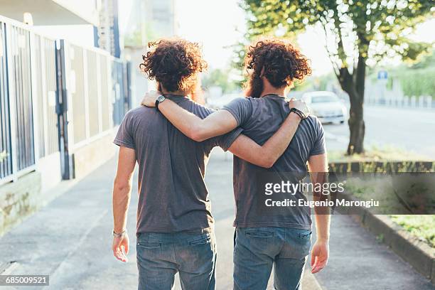 rear view of identical male adult twins strolling on sidewalk - tweeling stockfoto's en -beelden