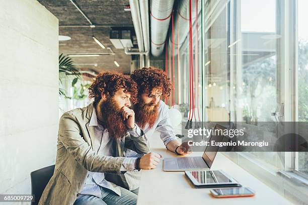 male adult hipster twins pointing at laptop in office - twin day outfit ideas fotografías e imágenes de stock
