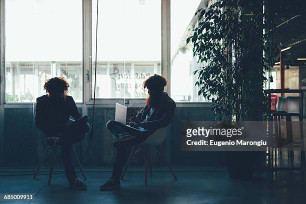 silhouetted male hipster twins working on laptop and digital tablet in office - digital twin bildbanksfoton och bilder