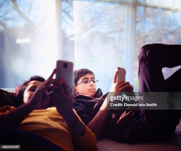 mixed race brother and sister texting on cell phones near window - palmerston north nz bildbanksfoton och bilder