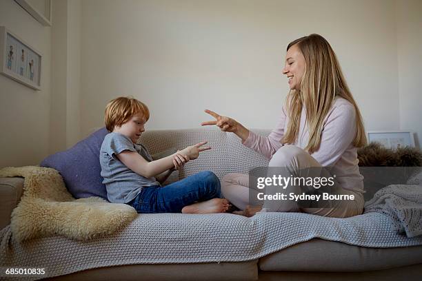 mid adult woman and son playing rock-paper-scissors on sofa - rock paper scissors stock pictures, royalty-free photos & images