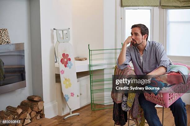 fed up mid adult man with basket of laundry in living room - chores stock pictures, royalty-free photos & images