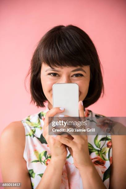 hispanic woman hiding face behind cell phone - flirting stockfoto's en -beelden