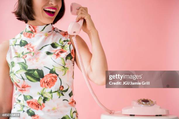 hispanic woman wearing floral dress holding pink telephone - landline phone woman stock pictures, royalty-free photos & images