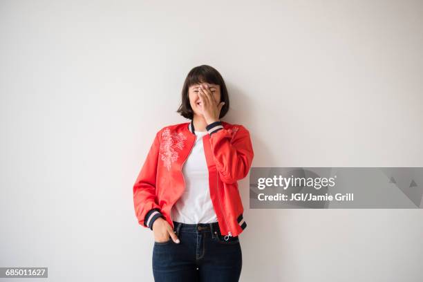 laughing hispanic woman wearing red jacket leaning on wall - manos a la cabeza fotografías e imágenes de stock