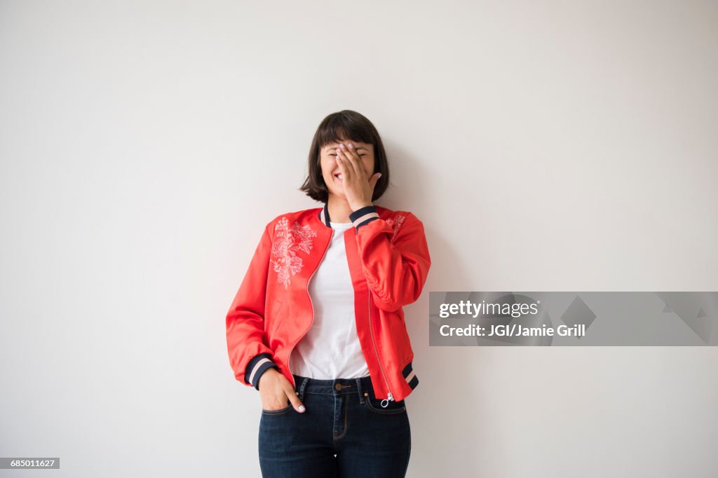 Laughing Hispanic woman wearing red jacket leaning on wall