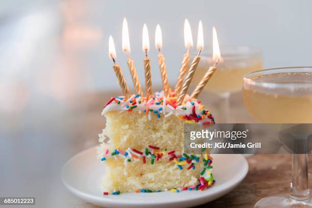 candles burning on slice of cake with sprinkles near champagne - cake slices stock-fotos und bilder