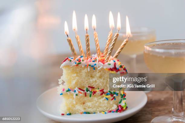 candles burning on slice of cake with sprinkles near champagne - pastel de cumpleaños fotografías e imágenes de stock
