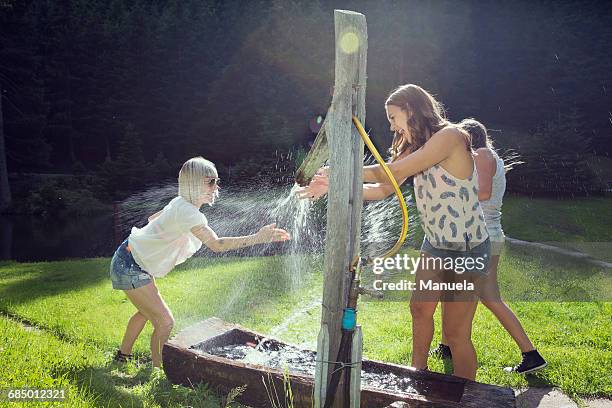 three adult female friends play fighting sprinkling water hose in garden - women in wet tee shirts stock pictures, royalty-free photos & images