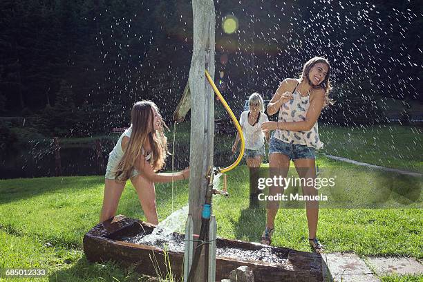 three adult female friends play fighting with water hose in garden - tirol deelstaat stockfoto's en -beelden