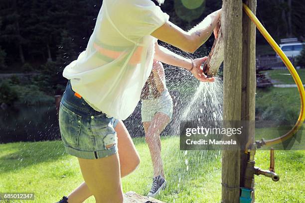 two adult female friends play fighting sprinkling water hose in garden - tirol deelstaat stockfoto's en -beelden