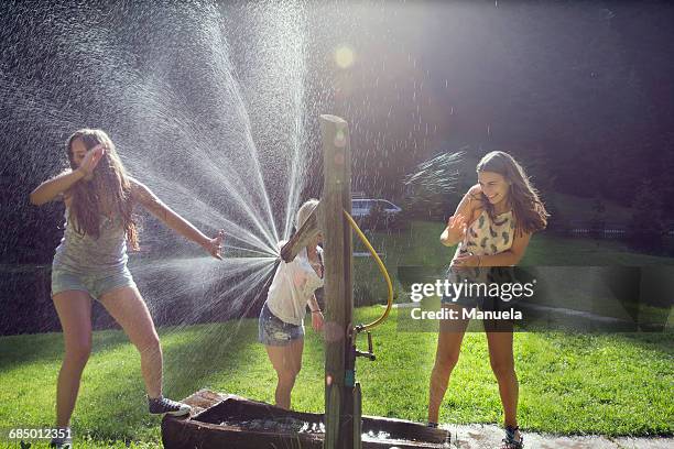 three adult female friends play fighting sprinkling water hose in garden - tirol deelstaat stockfoto's en -beelden