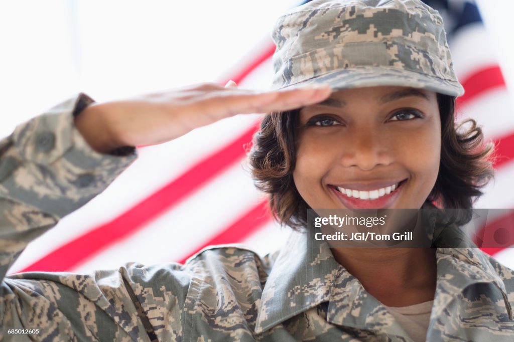 Portrait of smiling Mixed Race soldier saluting near American flag