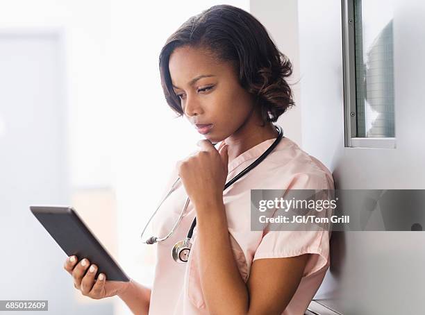 mixed race nurse using digital tablet leaning on door - nurse thinking stock pictures, royalty-free photos & images