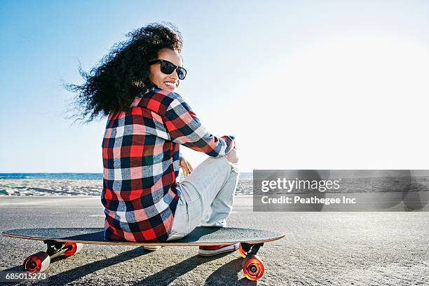 hispanic woman sitting on skateboard at beach - manhattan beach stockfoto's en -beelden