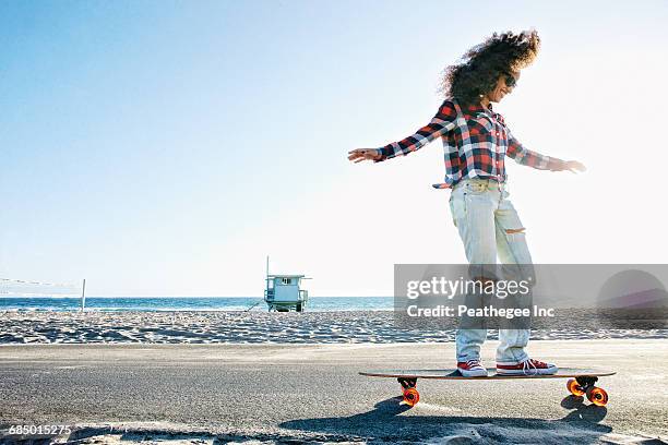 hispanic woman riding skateboard at beach - manhattan beach stock-fotos und bilder