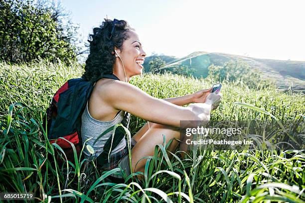 smiling mixed race woman sitting on hill listening to cell phone - woman smartphone nature stockfoto's en -beelden